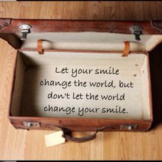 an open suitcase sitting on top of a wooden floor next to a sign that says let your smile change the world, but don't let the world change your smile