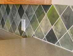 a kitchen counter with green and grey tiles on the backsplash, next to a light switch