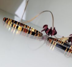 two gold and black bracelets sitting on top of a white table next to flowers