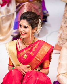 a woman sitting on the ground wearing a red and gold sari