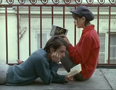 two people sitting on the ground with one reading a book while the other is laying down