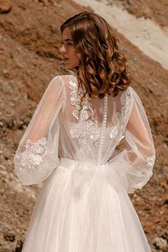 a woman in a white wedding dress standing on the side of a rocky hill with her back to the camera