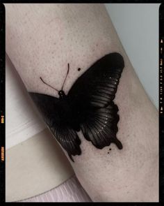 a black butterfly tattoo on the arm