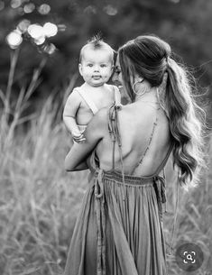 a woman holding a baby in her arms and looking at the sky with trees in the background