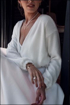 a woman sitting down wearing a white sweater and ring on her left hand, looking off to the side