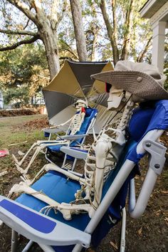 two lawn chairs with hats and umbrellas on them sitting in front of a house