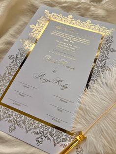 a wedding card with gold foil on it and a feather quill next to it