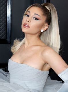 a woman with long blonde hair wearing a white dress and diamond earrings, posing for the camera