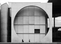 black and white photograph of two people walking in front of a building with circular windows