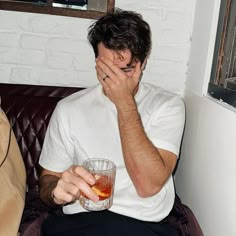 a man sitting on a couch holding his face to his mouth with a drink in front of him