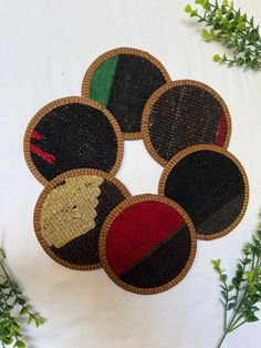 four woven coasters with different designs on them sitting next to some green plants and greenery