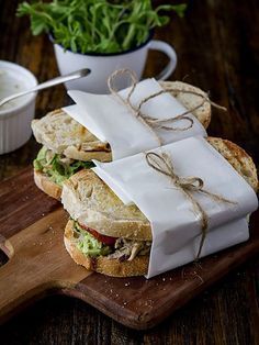 two sandwiches wrapped in white paper sitting on top of a wooden cutting board