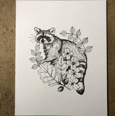 a black and white drawing of a raccoon surrounded by flowers on a sheet of paper