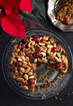 a pie with nuts and cranberries is on a glass plate next to a red poinsetti