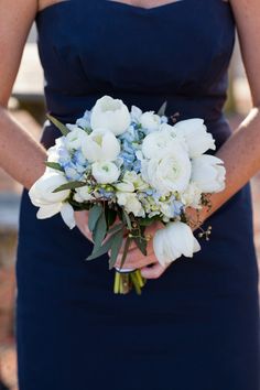 a woman in a blue dress holding a bouquet of white and blue flowers on her wedding day