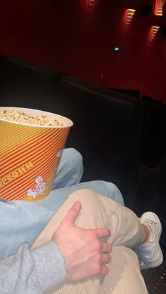 a person sitting in a chair with a popcorn bucket on their lap and thumbs up