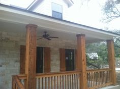 the front porch of a house with wooden pillars and shutters on each side, along with a ceiling fan