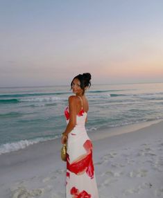 a woman in a red and white dress standing on the beach