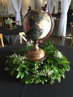 a globe on top of a table surrounded by greenery and white flowers in a banquet hall