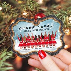 someone holding up a cheer squad ornament in front of a christmas tree with lights