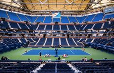 the inside of a tennis stadium with blue seats and people playing tennis on the court