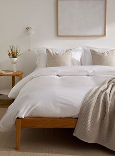 a bed with white linens and pillows in a small room next to a painting on the wall