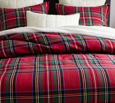 a bed with red and green plaid comforter on top of it, next to pillows