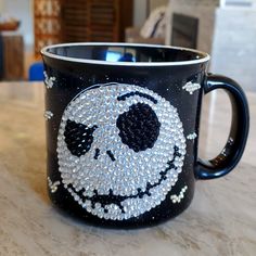 a black coffee mug with a skull on it's side and some silver beads around the rim