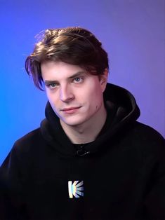 a young man in a black hoodie posing for a photo with blue background and light reflection