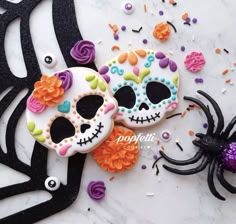 two decorated sugar skulls sitting on top of a table next to a purple and orange spider