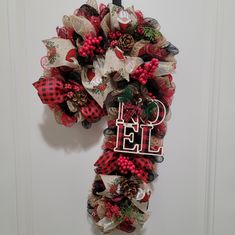 a red and black wreath hanging on the front door with monogrammed letters that spell out noel