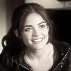 a black and white photo of a woman with long hair smiling at the camera while wearing a leather jacket