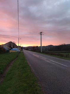 the sun is setting on an empty road near some grass and power lines in the distance