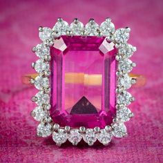 An imposing Art Deco style cocktail ring built around a large emerald cut pink topaz, weighing an impressive 9 carats (approx.) It's framed by twinkling brilliant cut cubic zirconia around the border which complement the vivid pink hue beautifully.   Pink topaz comes in shades of soft pink or fiery red and like a ruby is considered a stone of the heart. A symbol of femininity and romance, it's said to bring good fortune in love, providing happiness and vitality to any relationship. The rectangul Luxury Pink Topaz Ring For Formal Occasions, Elegant Pink Topaz Ring For Formal Occasions, Dazzling Pink Emerald Cut Ring, Pink Emerald-cut Diamond Ring With Halo Setting, Pink Diamond Ring With Emerald Cut And Halo Setting, Elegant Pink Emerald-cut Ruby Ring, Elegant Hallmarked Pink Diamond Ring, Elegant Pink Emerald Cut Ruby Ring, Pink Emerald Cut Diamond Ring With Halo Setting