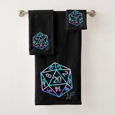 two black towels with neon colored dices on them hanging from a towel rack in front of a white wall