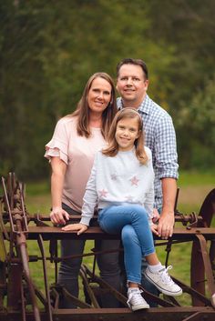 a man, woman and child sitting on an old farm equipment