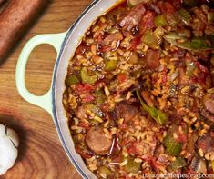 a pot filled with rice and sausage next to a wooden spoon on top of a table