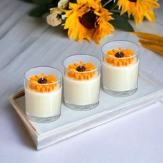 three small glasses filled with milk and orange flowers on a tray next to sunflowers