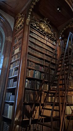 an old library filled with lots of books next to a tall wooden staircase in front of a window