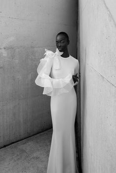 a woman in a white dress leaning against a wall