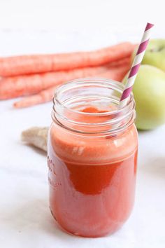 carrots and apples are sitting next to a mason jar with a straw in it