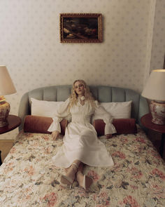 a woman sitting on top of a bed in a room with floral bedspread