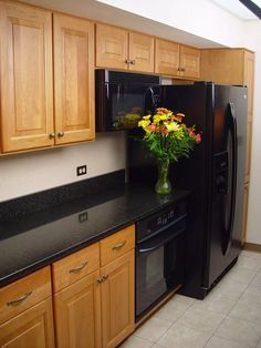 a black refrigerator freezer sitting inside of a kitchen next to wooden cabinets and drawers