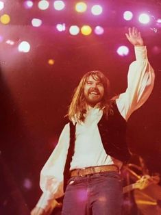 a man with long hair and beard standing on stage holding his arms up in the air