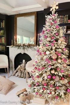 a white christmas tree with pink and gold ornaments in front of a fireplace mantel