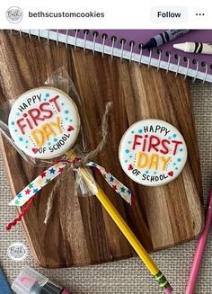 two decorated cookies sitting on top of a wooden cutting board next to pencils and markers