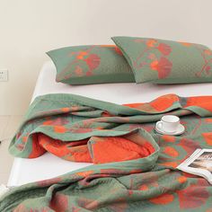 an orange and green blanket on top of a bed next to two teacups