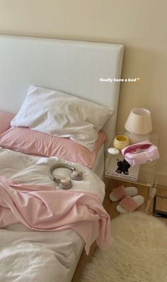 a white bed with pink sheets and pillows on top of it next to a lamp