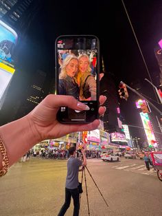 a person holding up a cell phone to take a selfie in times square at night