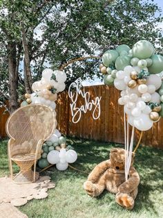 a teddy bear sitting in the grass next to balloons that spell out baby on it